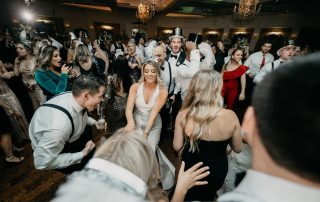 A large group of people dressed in formalwear and New Year’s accessories dance and celebrate together in a decorated indoor venue.