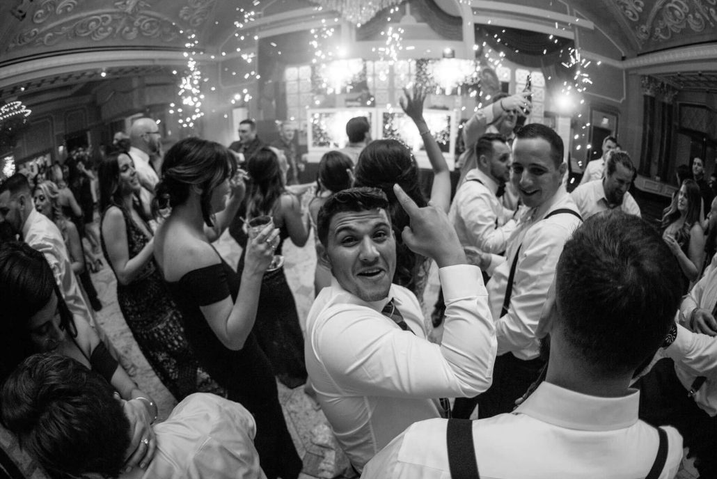 A group of people dressed formally dance and celebrate at an indoor event with sparklers and lights in the background.