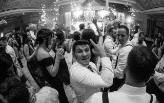 A group of people dressed formally dance and celebrate at an indoor event with sparklers and lights in the background.