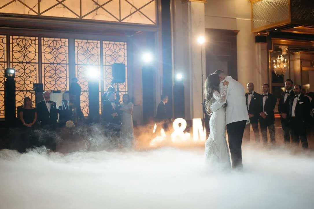 sce-central-nj-wedding-party-dj A bride and groom share their first dance in a fog-filled ballroom, surrounded by wedding guests and illuminated letters in the background.