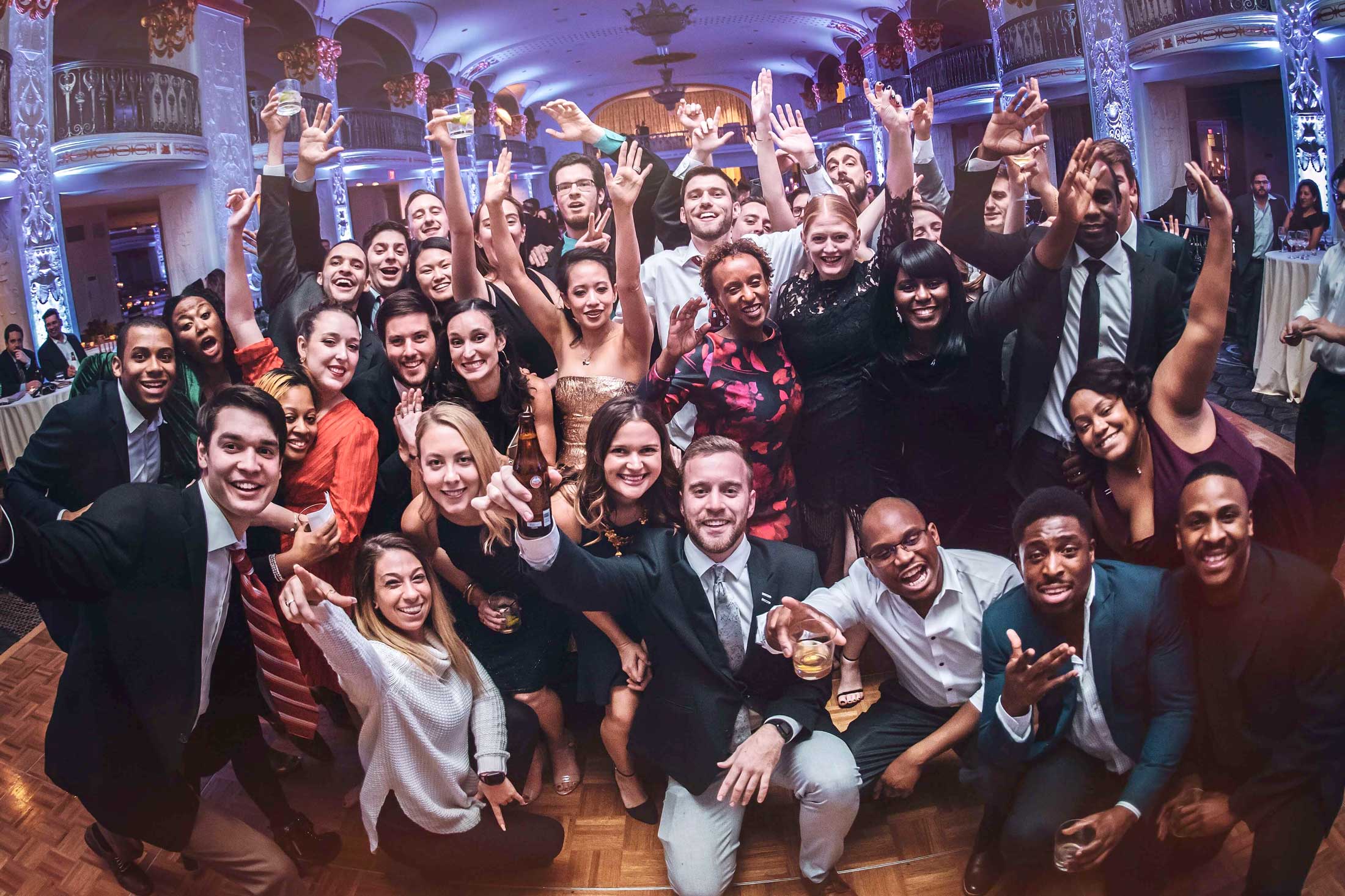 A large group of people dressed formally pose together and smile for a photo at an indoor event or celebration.