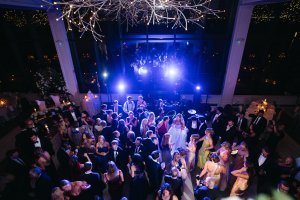 Overhead view of a formal party with many people dancing under bright lights in a large, decorated room at night.